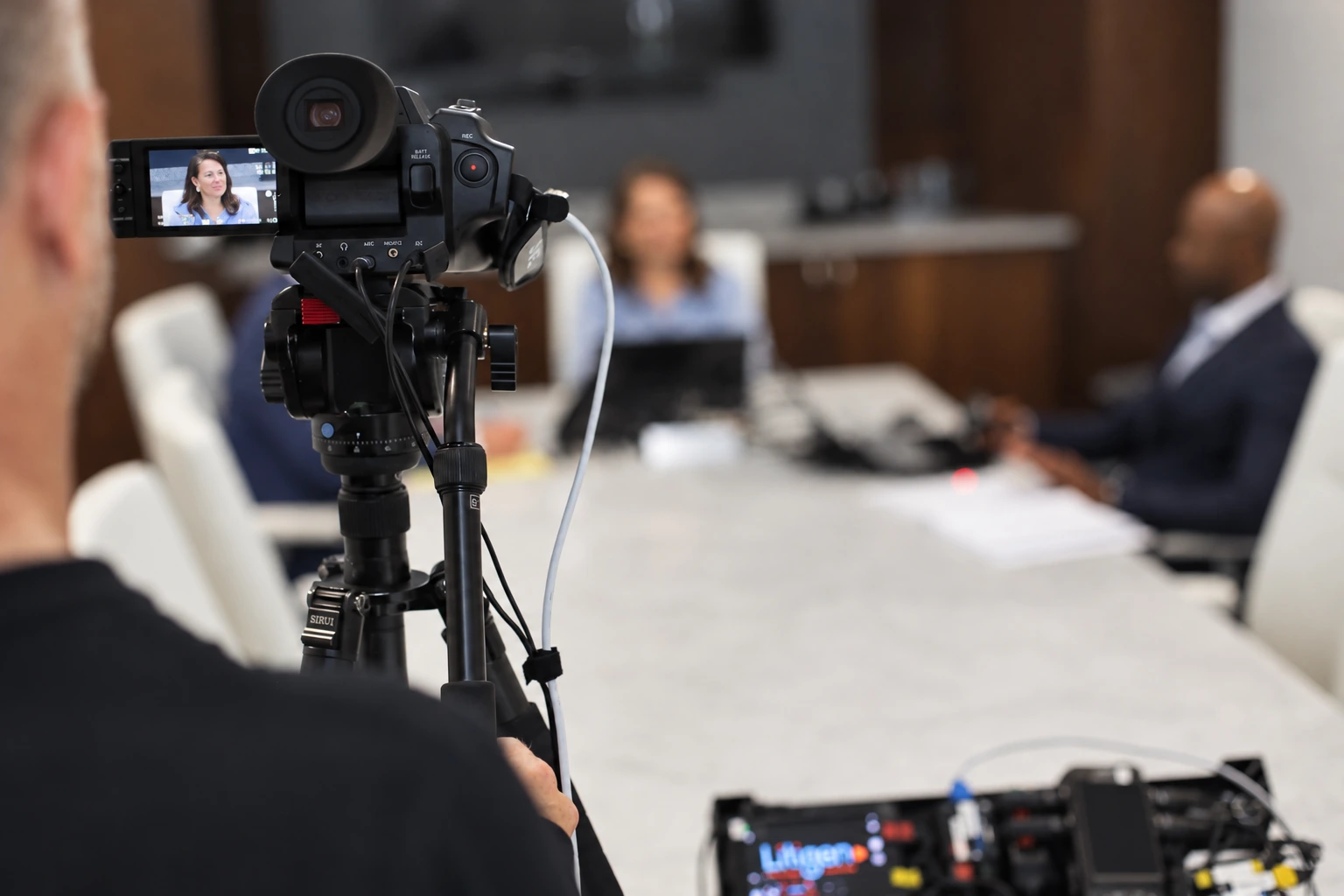 Camera and operator recording a deposition across a conference table, with the witness visible on the camera monitor.